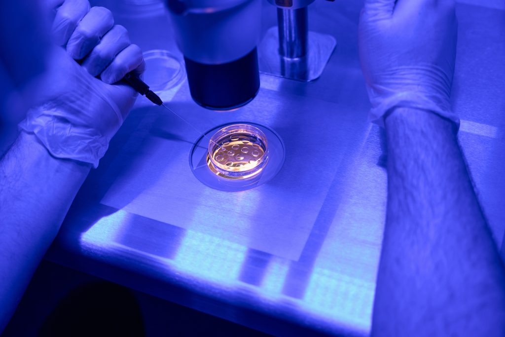 A man in a lab coat performing a biopsy on an embryo in an IVF laboratory, using specialized equipment under a microscope.